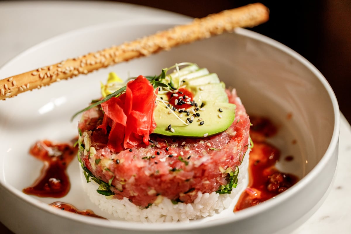 Gourmet tuna tartare appetizer plated on white with avocado, pickled ginger, microgreens, and sesame breadstick