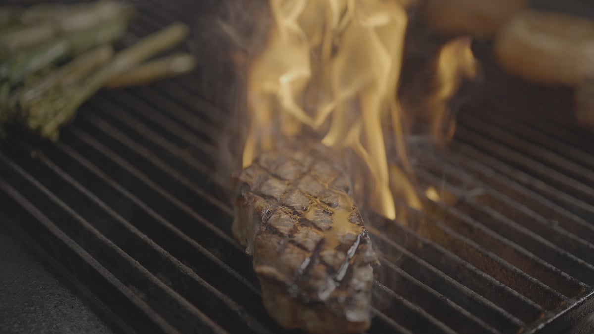 Grilled steak with flames cooking on a barbecue grill grate, ungraded original footage before the CW WARM LUT