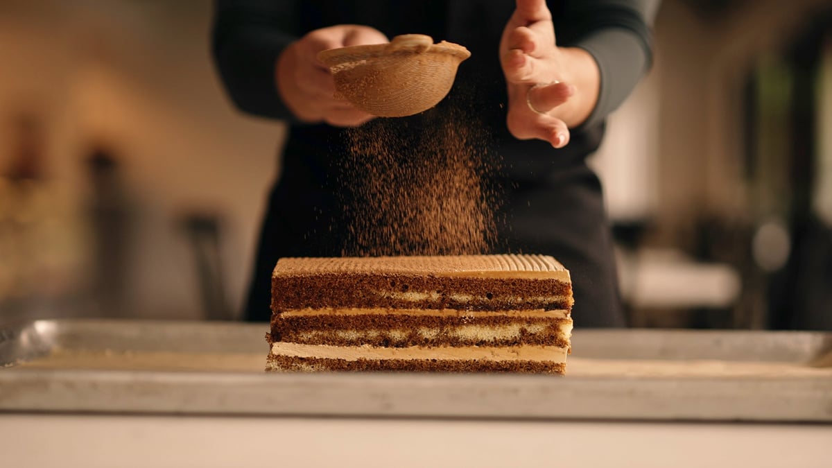 Chef dusting cocoa powder over a layered chocolate cake on a kitchen counter, graded with the CW CONTRAST LUT