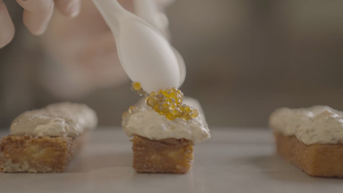 Piping white frosting onto small square cake pieces topped with gold edible glitter, ungraded original footage before the CW MAIN LUT