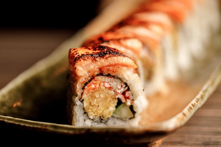Line of sushi rolls topped with seared salmon and sesame seeds on a ceramic plate