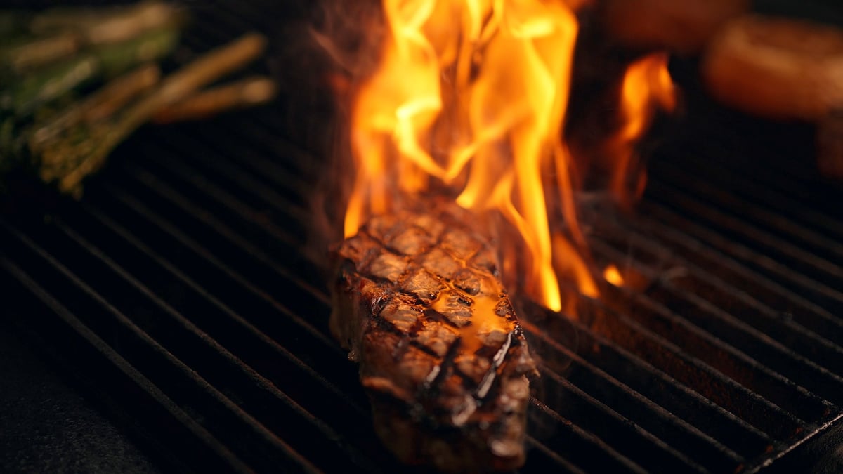 Steak cooking on a grill grates with flames and fire licking around the meat, graded with the CW WARM LUT