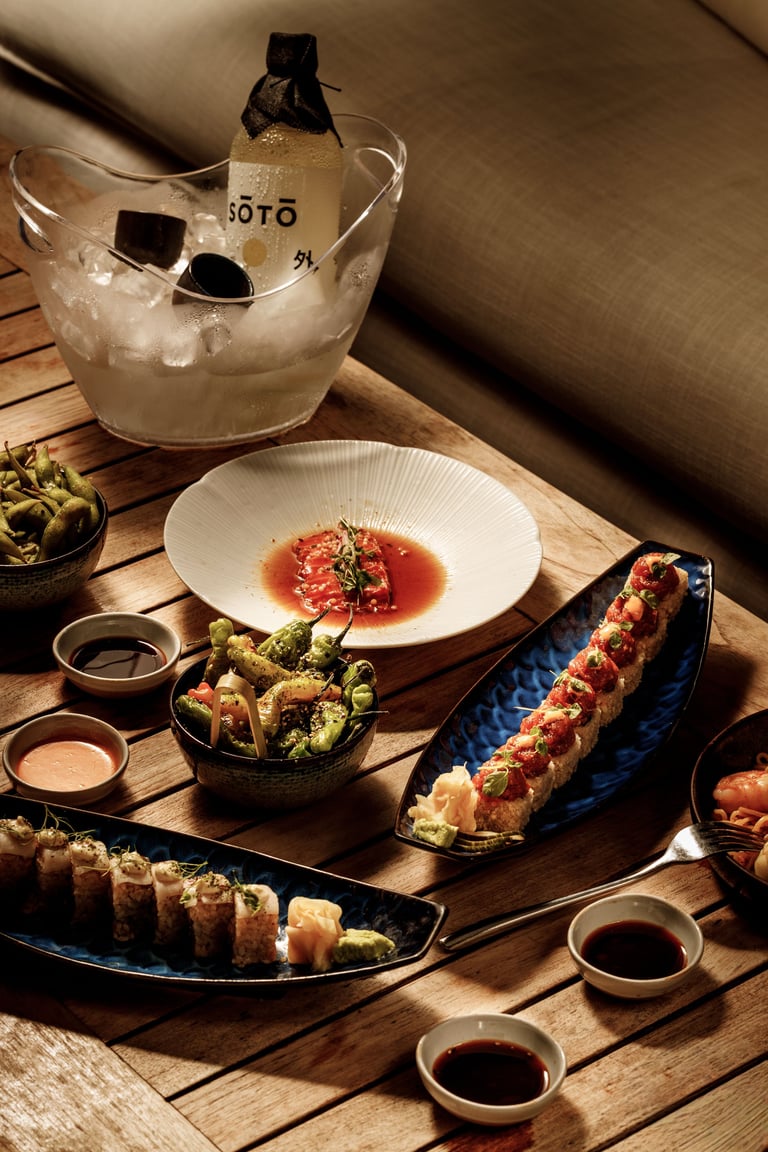 Japanese sushi platter with sake bottle in ice bucket, soy sauce, and wooden serving board with various sushi rolls and appetizers